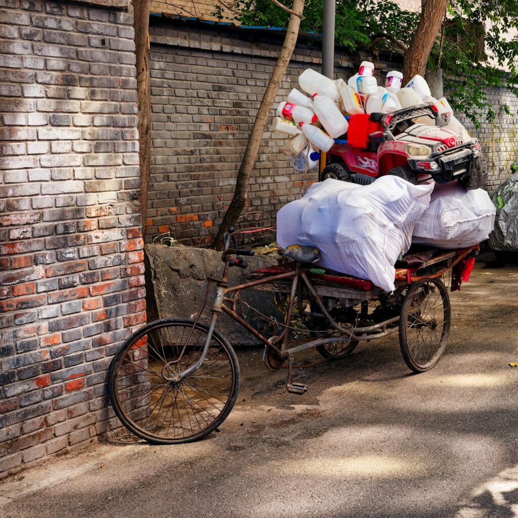 old bicycle cart loaded with plastic waste on a narrow city street surrounded by brick walls during daytime