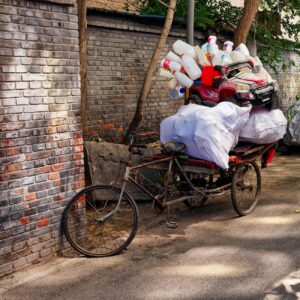old bicycle cart loaded with plastic waste on a narrow city street surrounded by brick walls during daytime