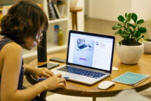 woman in black tank shirt facing a black laptop computer on brown wooden round table